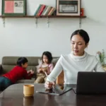 Moeder werkt thuis op haar laptop terwijl haar kinderen naast haar op de bank spelen