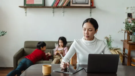 Moeder werkt thuis op haar laptop terwijl haar kinderen naast haar op de bank spelen