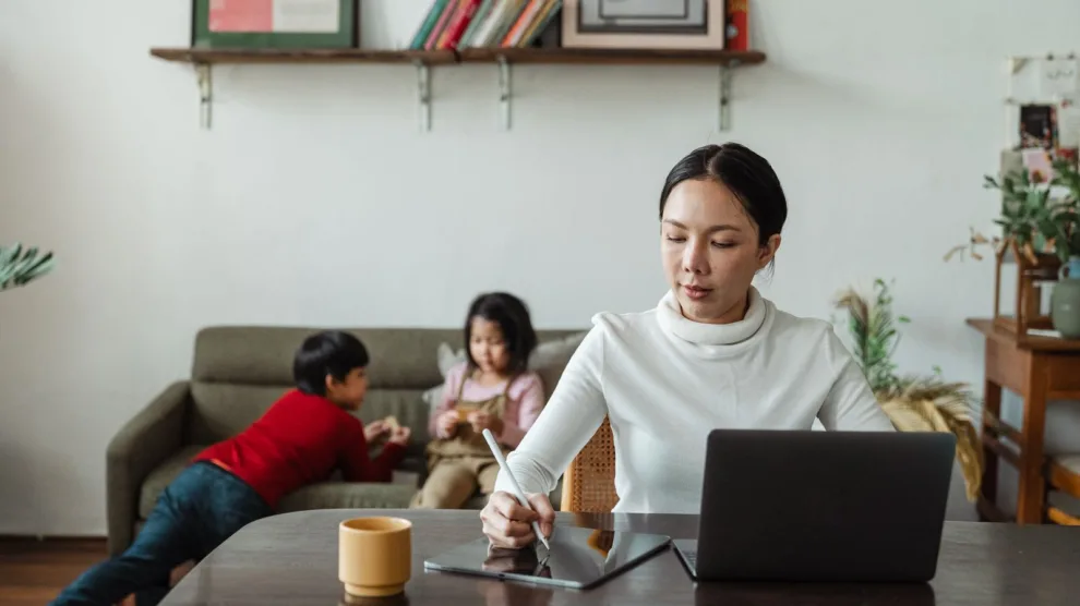 Moeder werkt thuis op haar laptop terwijl haar kinderen naast haar op de bank spelen