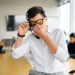 Vermoeide man met headset wrijft in zijn ogen op kantoor, een herkenbaar beeld van stress en vermoeide ogen