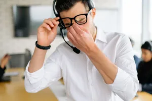 Vermoeide man met headset wrijft in zijn ogen op kantoor, een herkenbaar beeld van stress en vermoeide ogen
