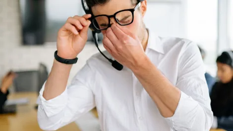 Vermoeide man met headset wrijft in zijn ogen op kantoor, een herkenbaar beeld van stress en vermoeide ogen