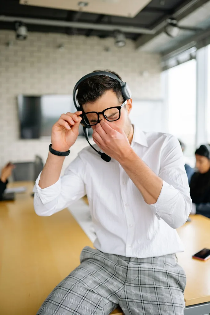 Vermoeide man met headset wrijft in zijn ogen op kantoor, een herkenbaar beeld van stress en vermoeide ogen